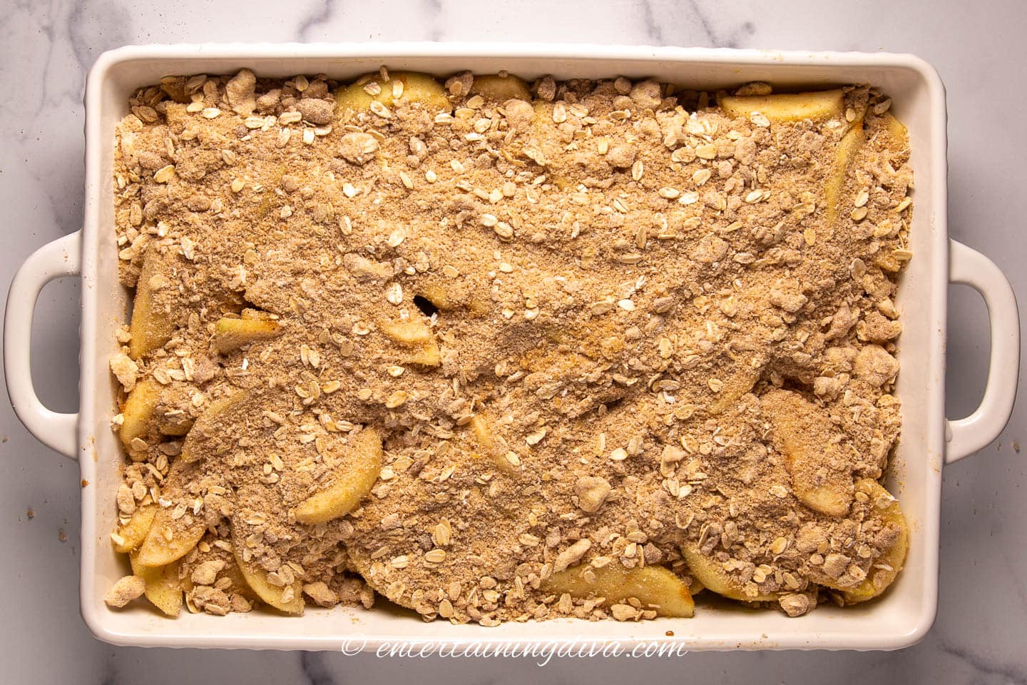 apples covered by oat topping in a baking dish before baking