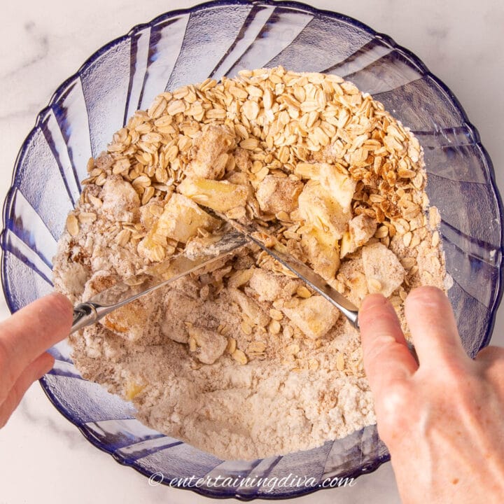 two knives cutting butter into rolled oats mixture