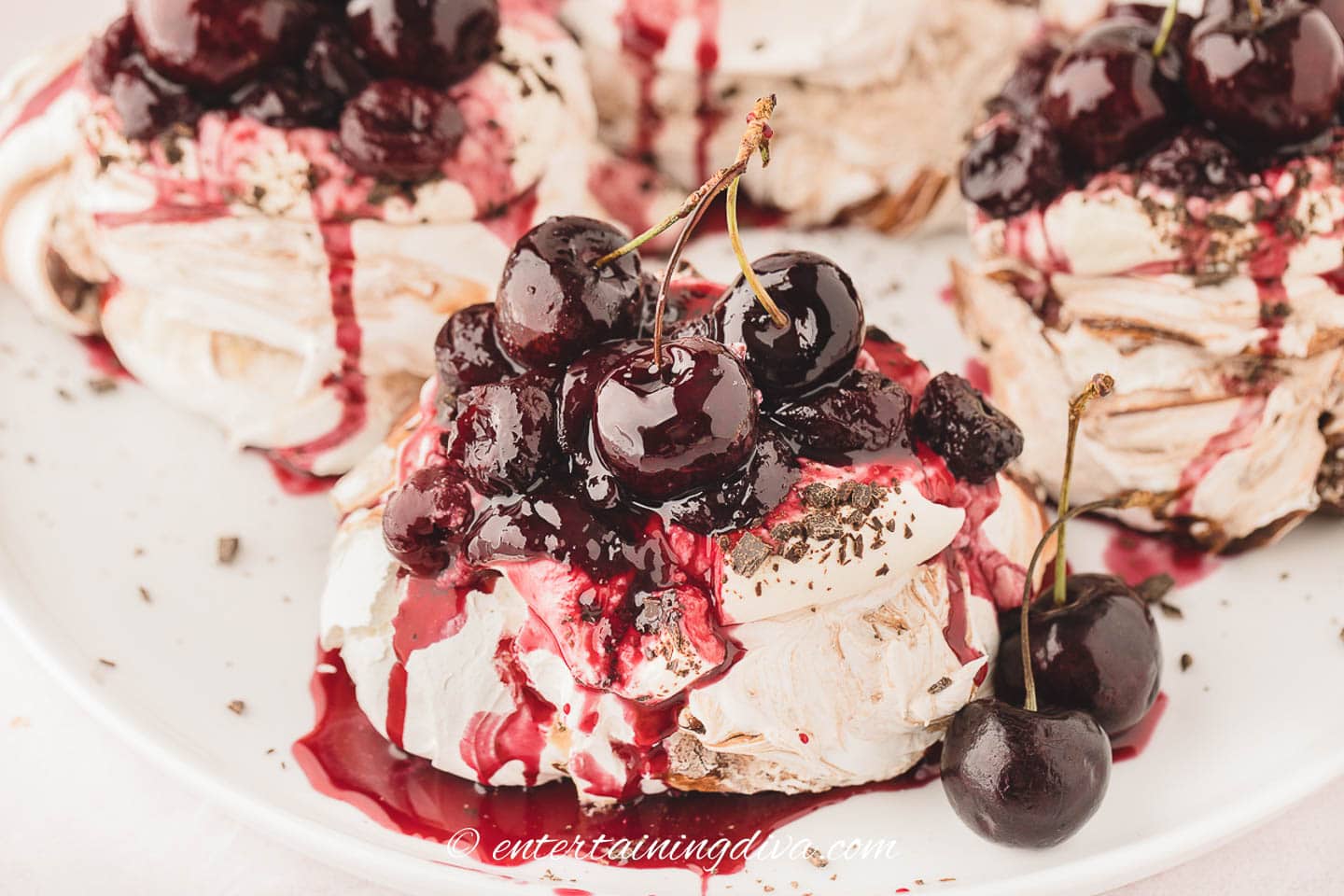 A black forest mini pavlova on a plate with cherries and other pavlovas
