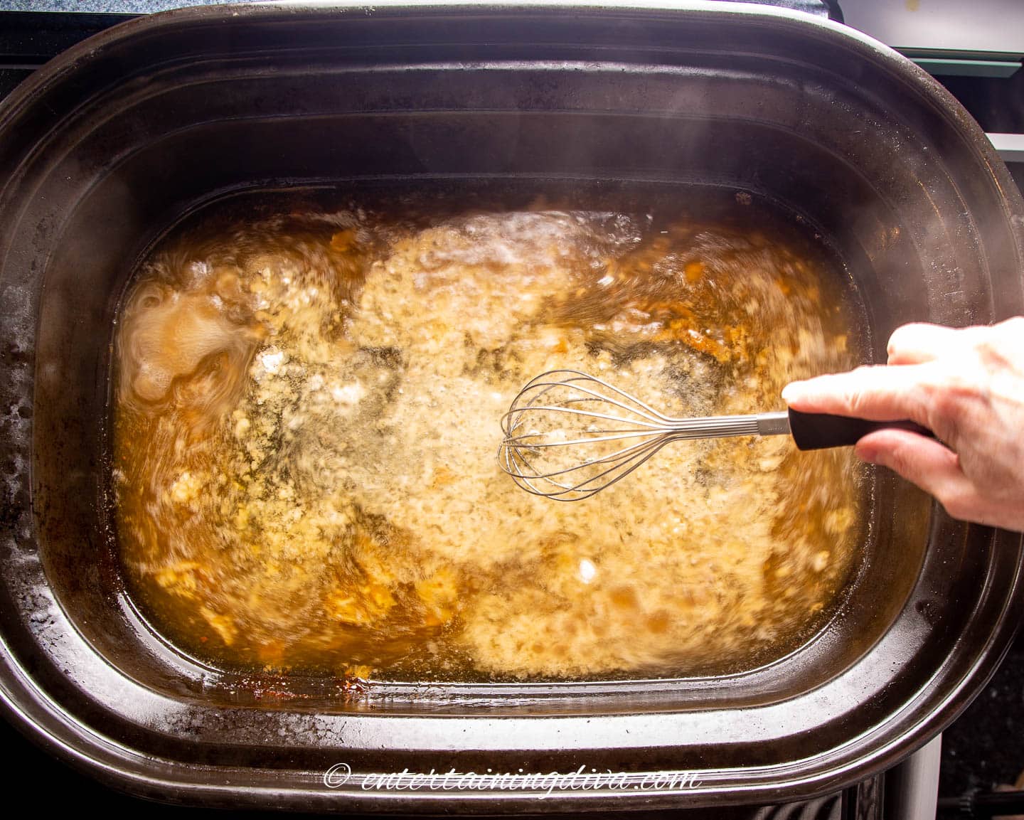 flour being whisked into turkey drippings in a roasting pan