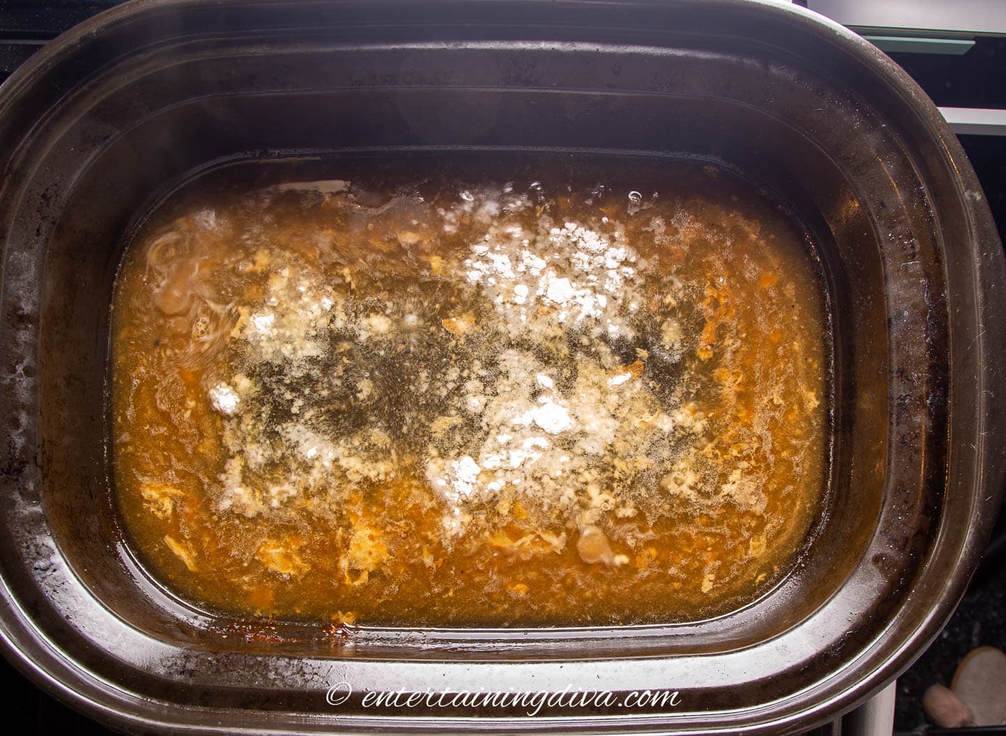 flour sprinkled on top of turkey drippings in a roasting pan