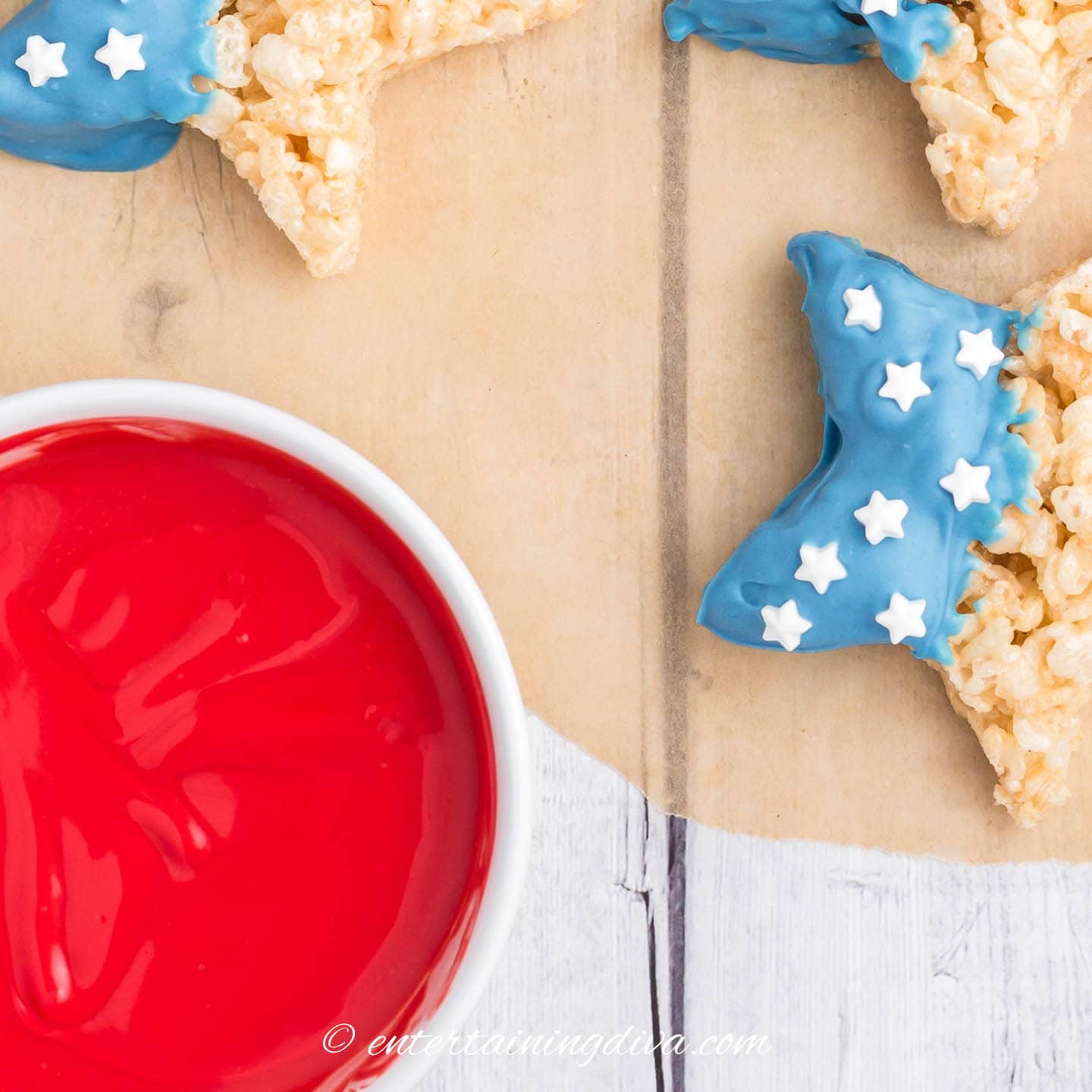 a bowl of melted red candy melts beside blue and white star-shaped rice krispie treats