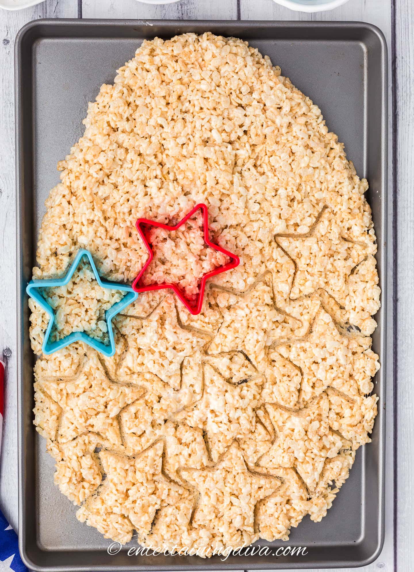 Star cookie cutters cutting Rice Krispie treats into star shapes on a baking sheet