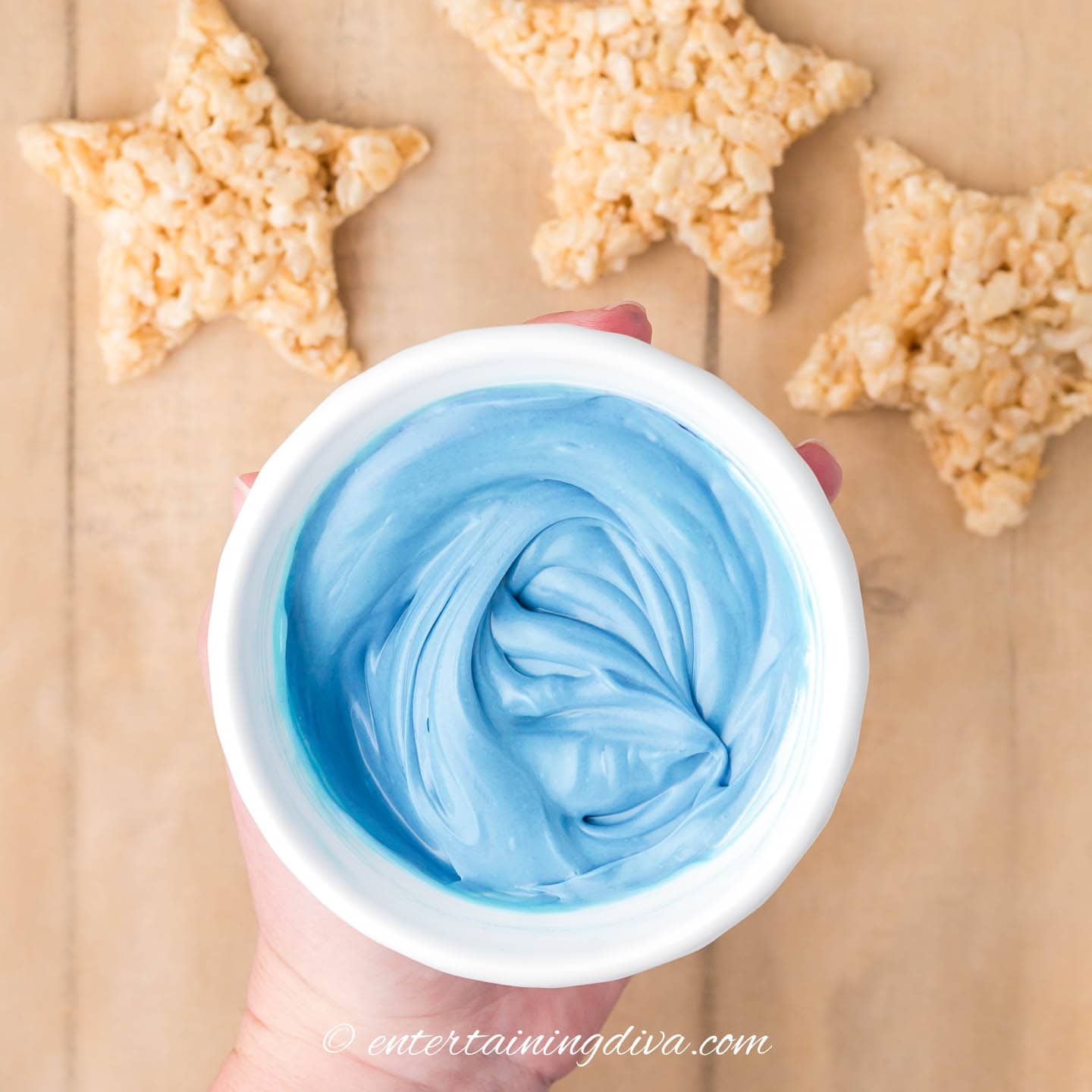 Melted blue candy melts in a bowl held up star-shaped rice krispie treats