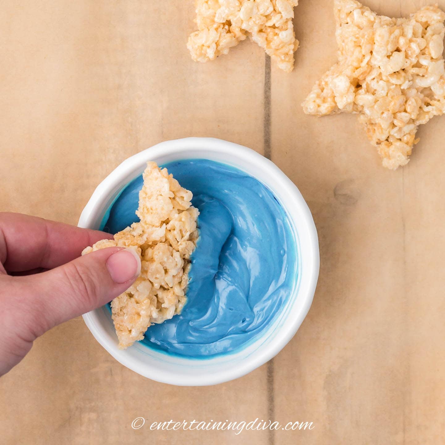 Star-shaped rice krispie treat being dipped in melted blue candy