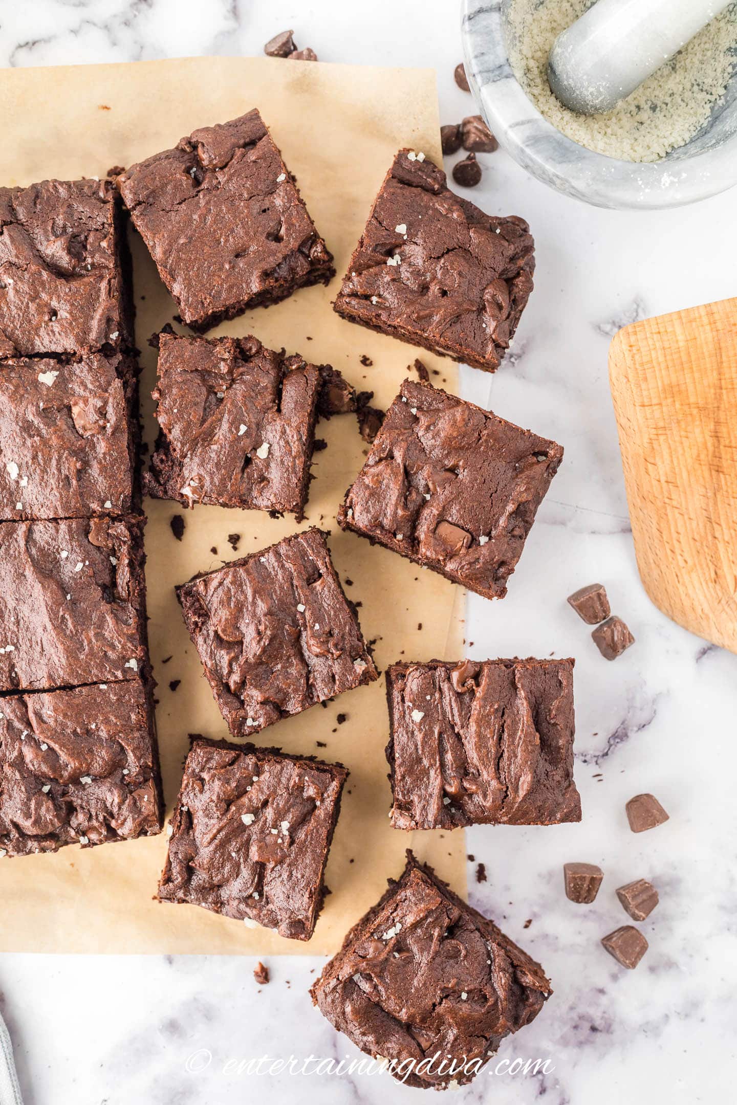 Many brownies spread out on a piece of parchment paper beside a bowl of coarse sea salt