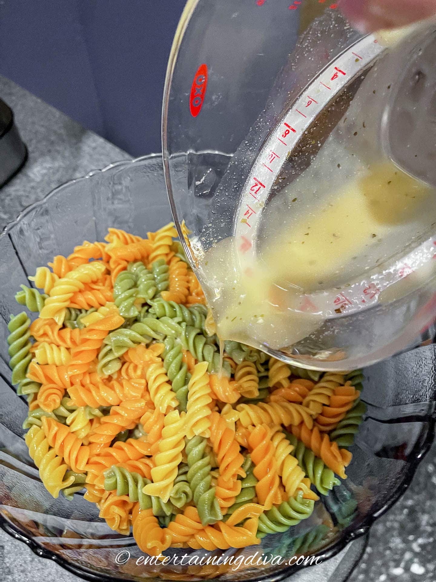 italian dressing benig poured over tricolor pasta
