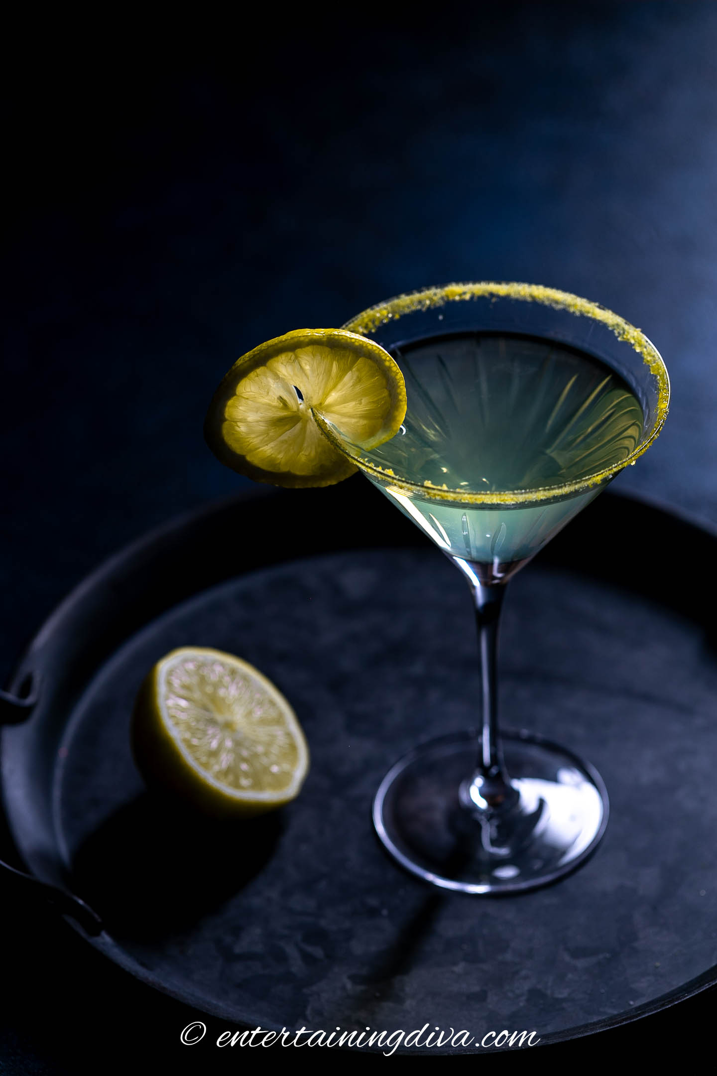 A limoncello martini on a tray with a slice of lemon.