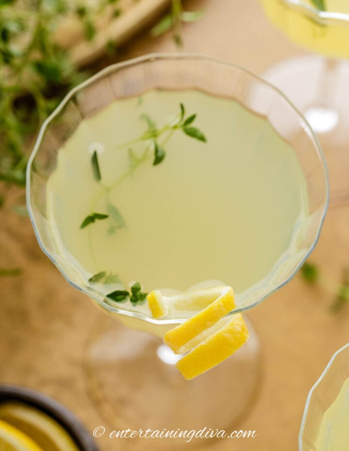 Overhead view of limoncello martini garnished with a twist of lemon and a sprig of thyme.