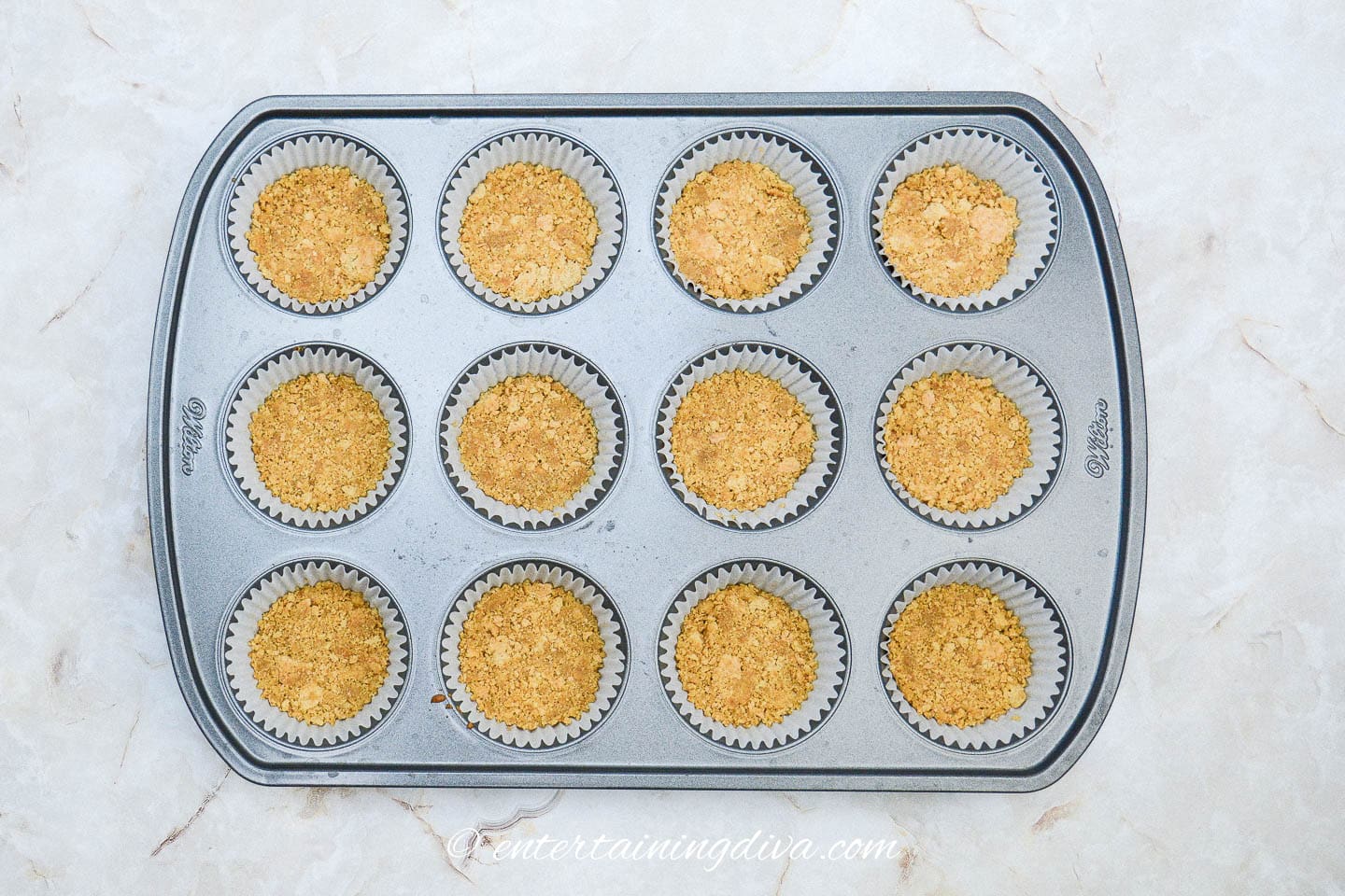 Graham cracker crust at the bottom of cupcake liners in a muffin tin