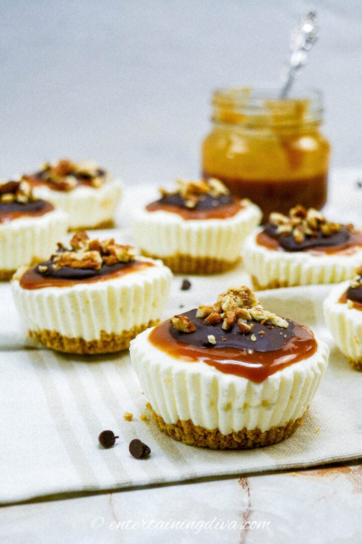 A tray of mini cheesecakes topped with caramel sauce, melted chocolate and nuts.