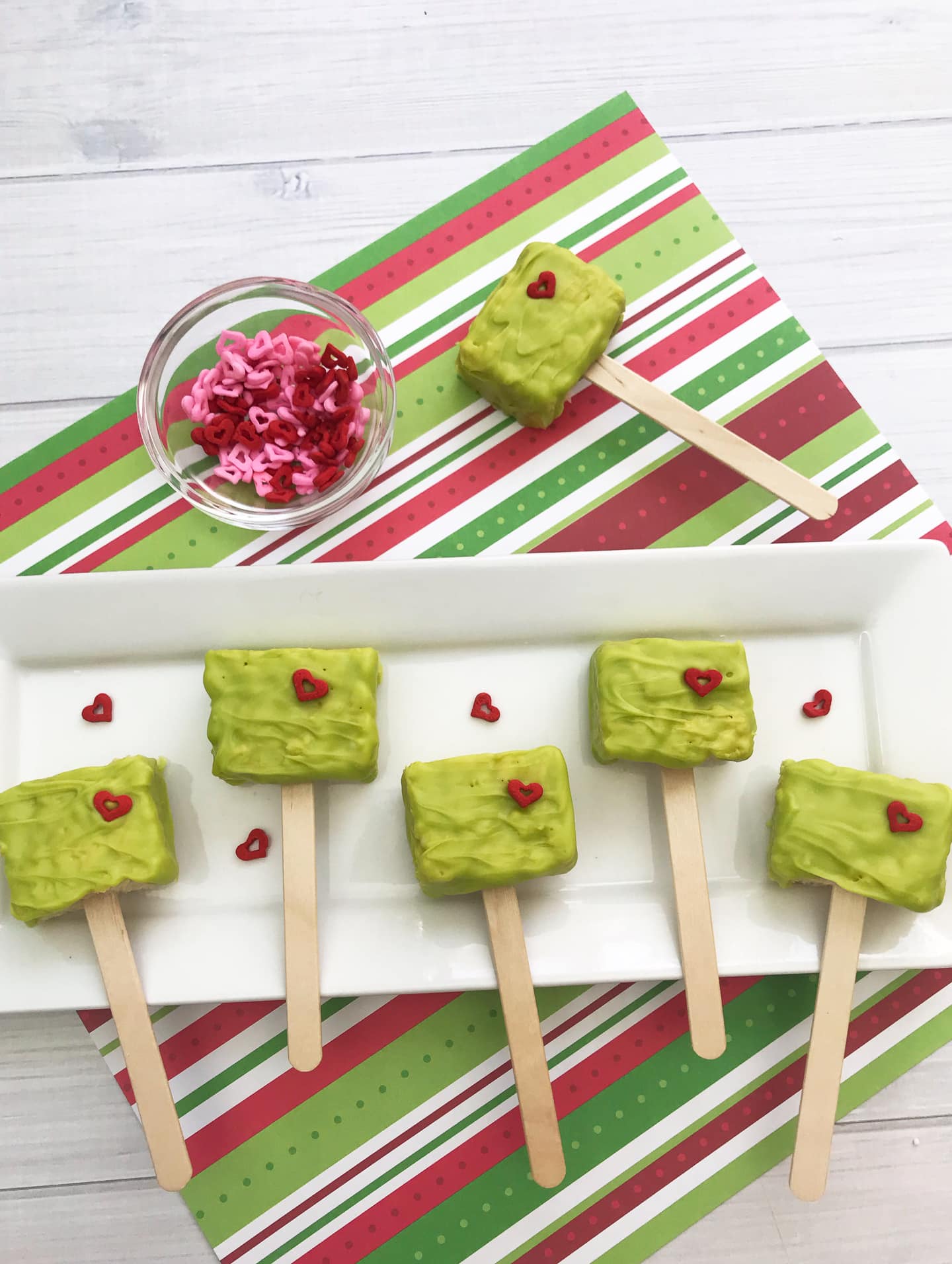 Green Grinch rice krispie pops on a plate with red heart decorations.