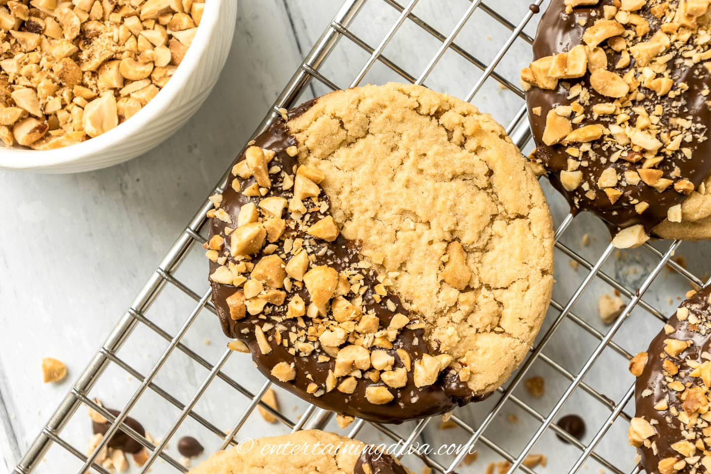 Chocolate-dipped peanut butter cookies topped with chopped peanuts on a cooling rack