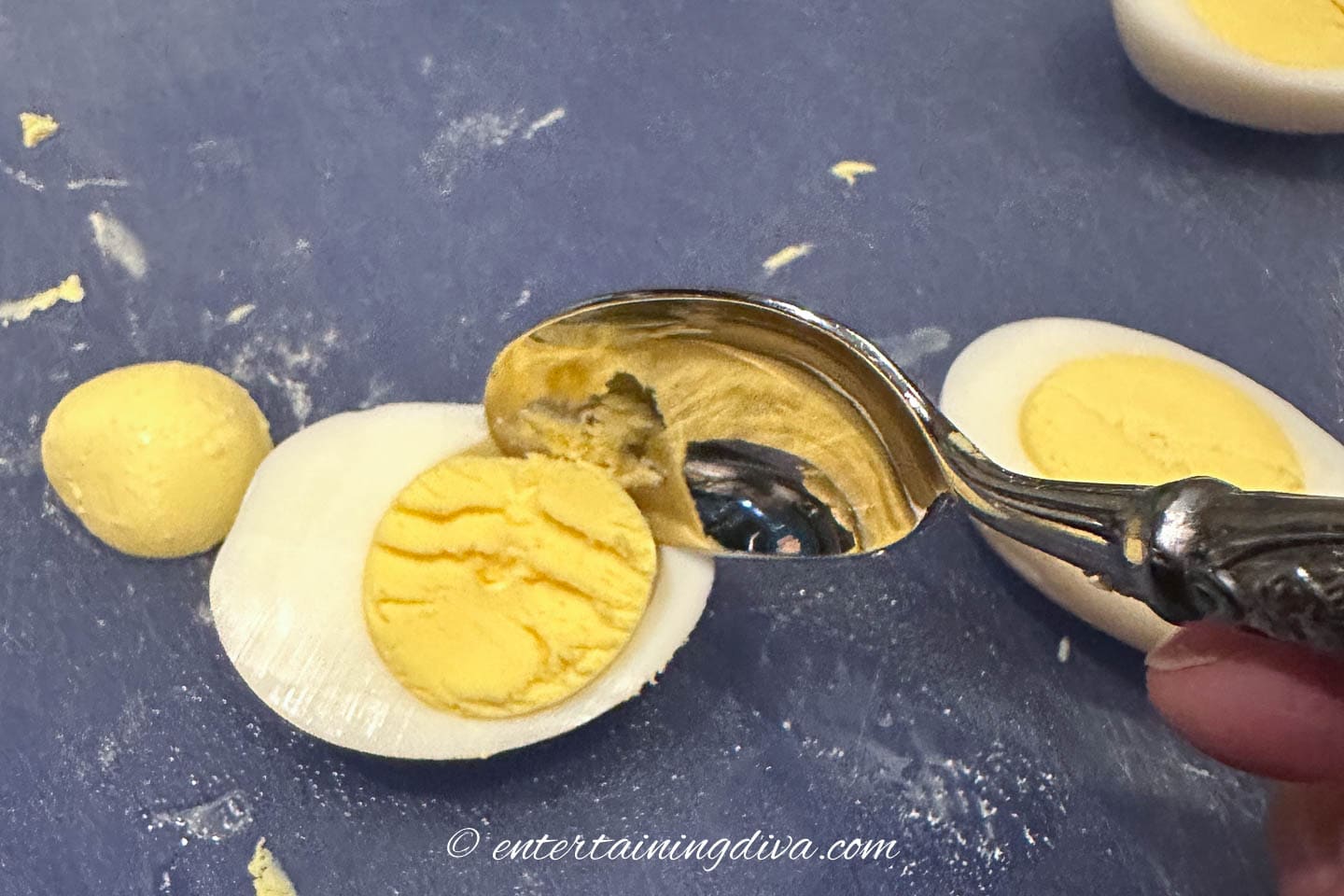 Yolk being scooped out of a hard boiled egg with a spoon