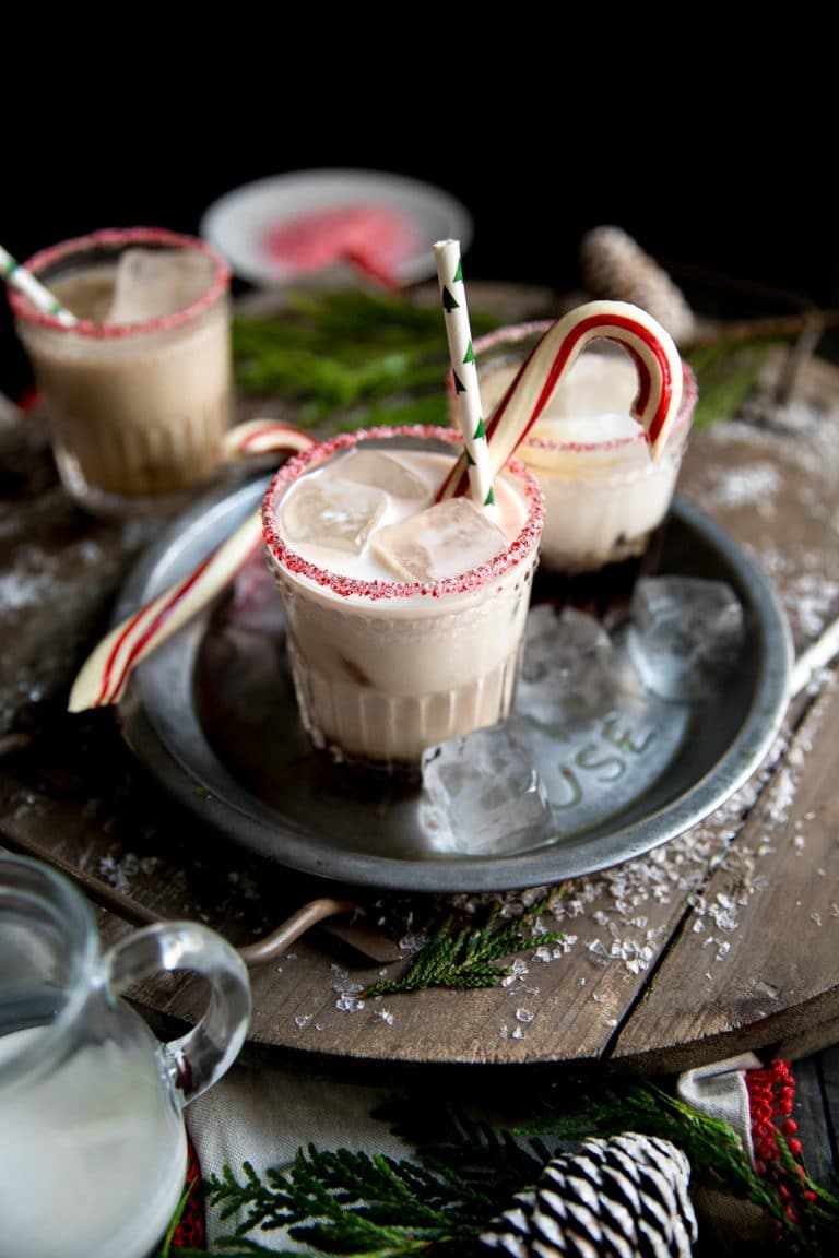 Peppermint white Russian Christmas cocktails with candy canes and ice cubes on a tray.