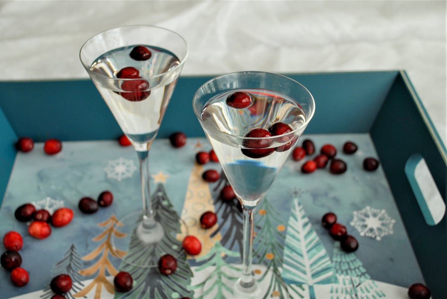 Two glasses filled with Clear Winter Cosmo and cranberries on a tray.