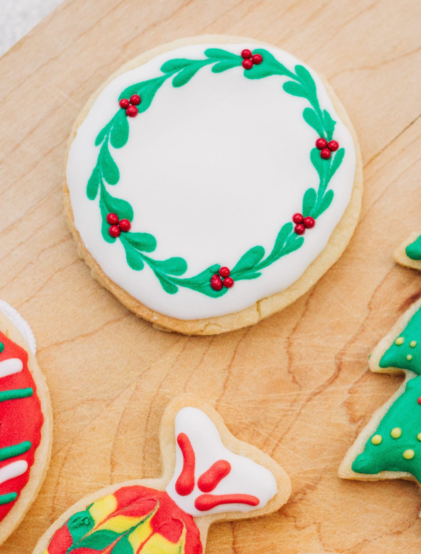Festively decorated wreath Christmas cookies on a wooden cutting board.