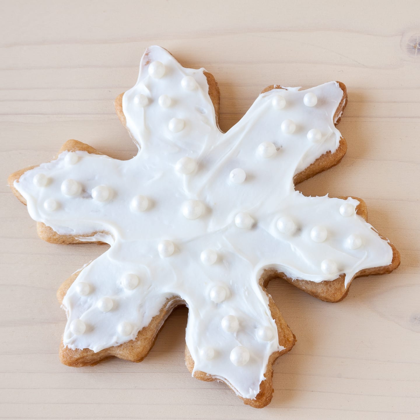 A snowflake cookie decorated with white icing and sugar pearls