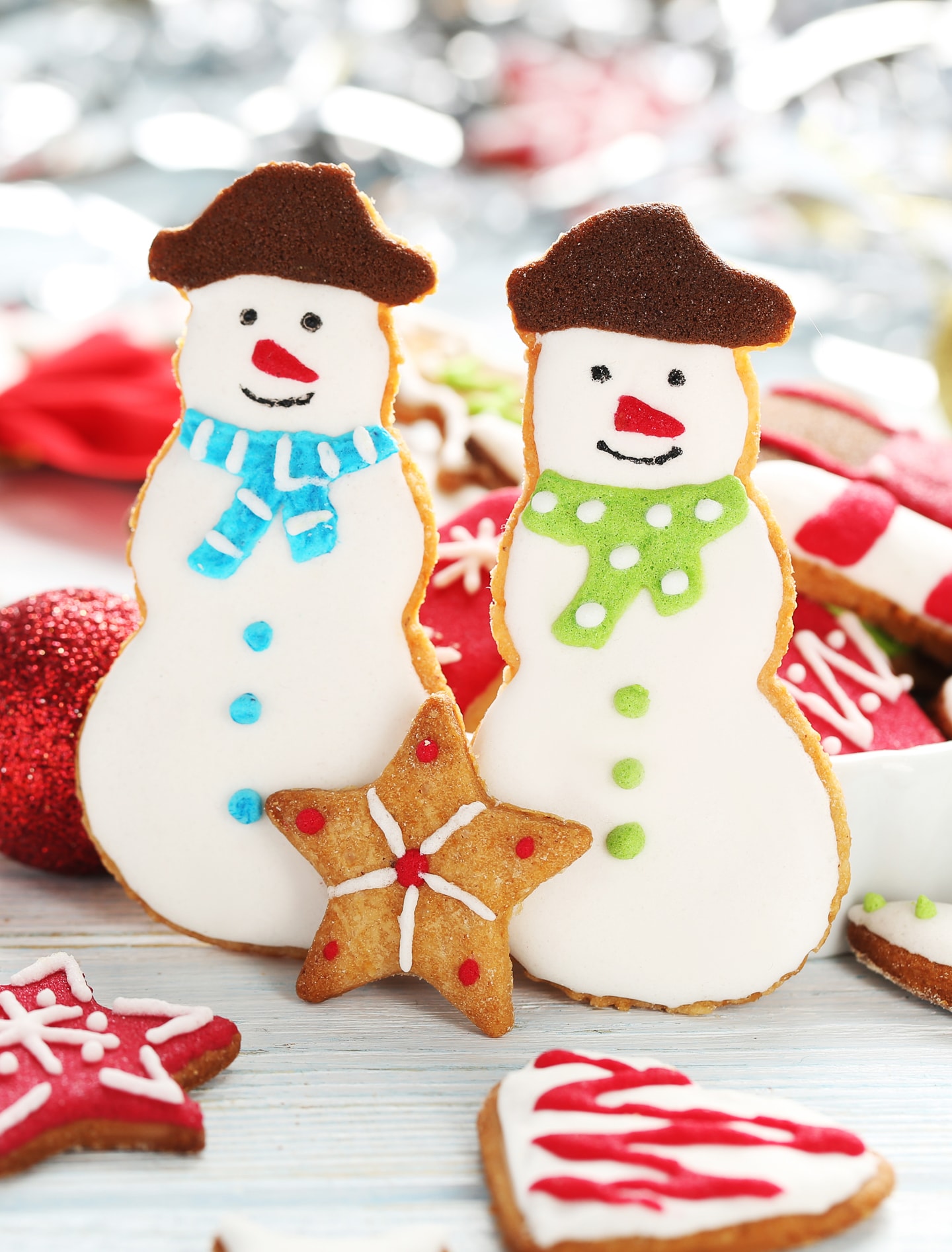Two decorated snowman cookies on a table with other cut out cookies.
