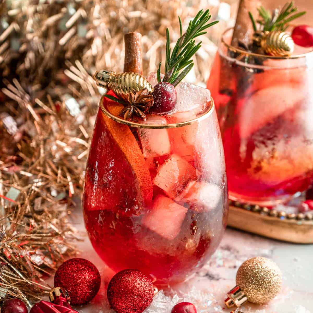 Two glasses of cranberry Aperol spritz garnished with cranberries, rosemary and a cinnamon stick