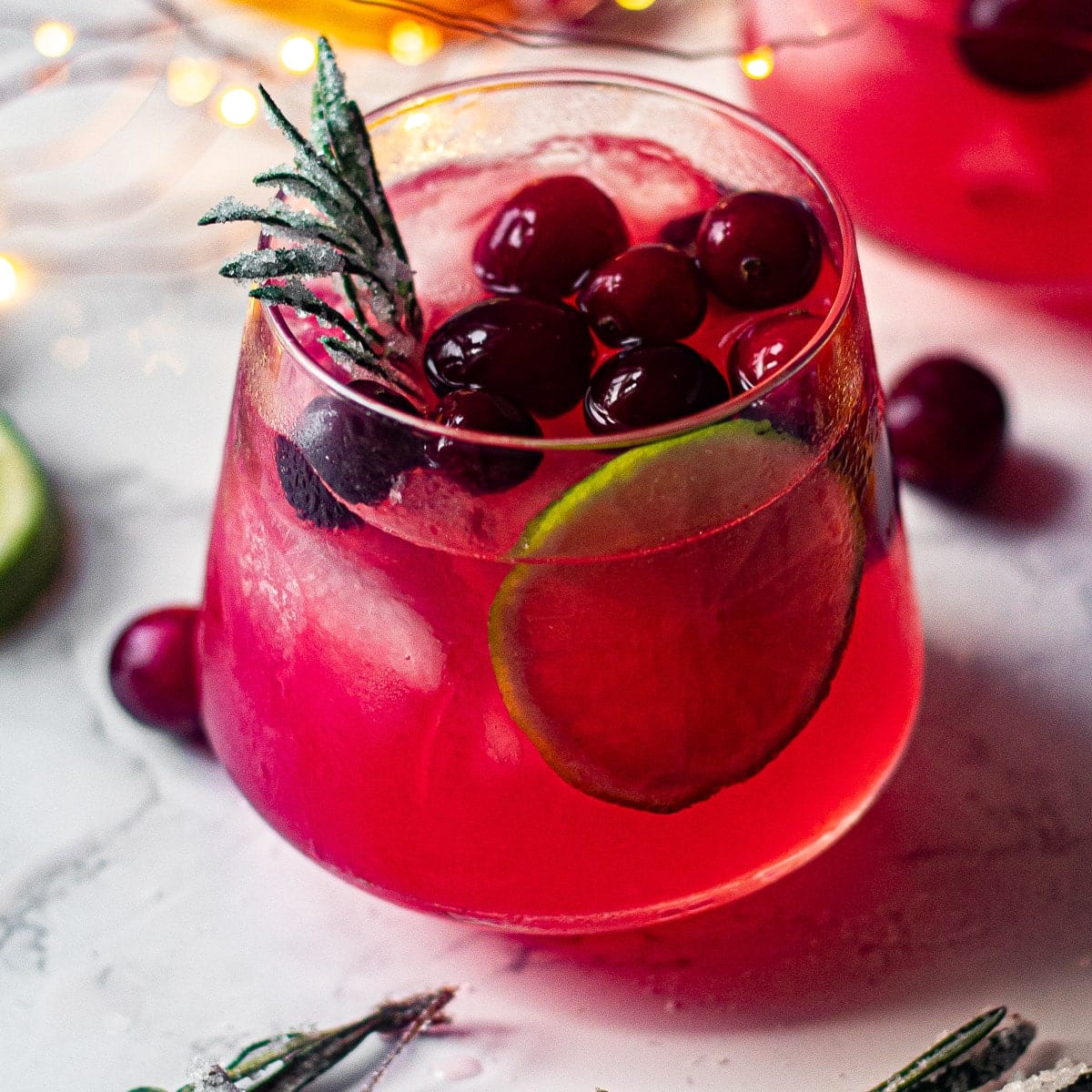 Cranberry margarita with lime and sprigs of rosemary.