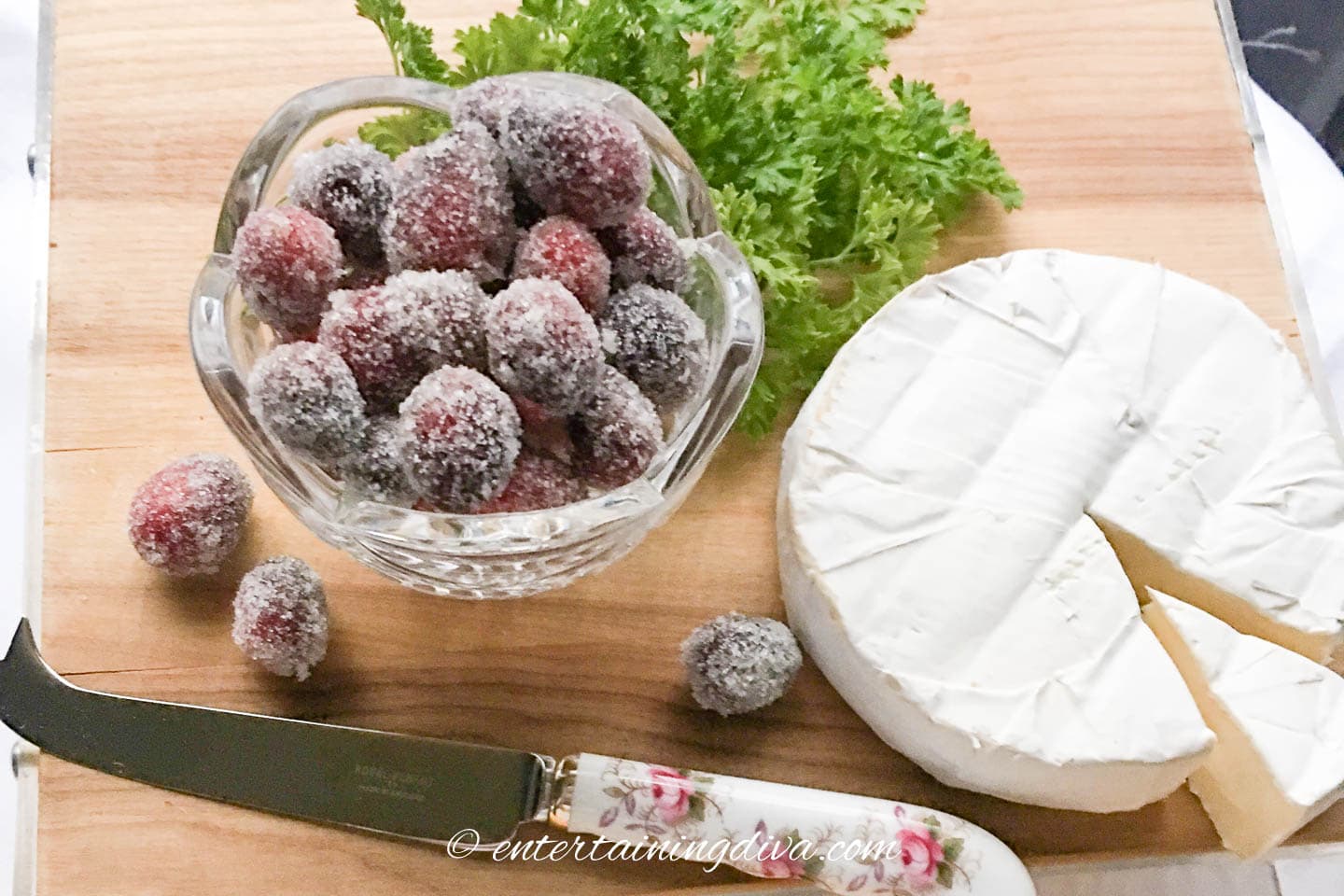 sugared cranberries on a cutting board with a piece of brie cheese