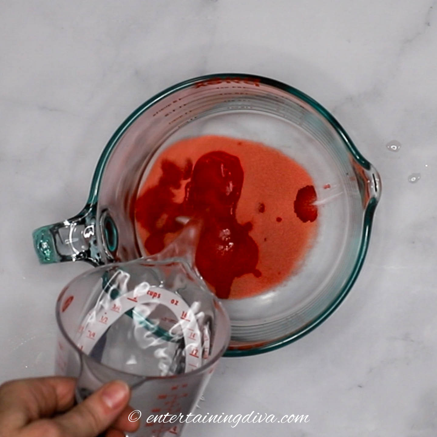 Hot water being poured into red jello crystals in a bowl