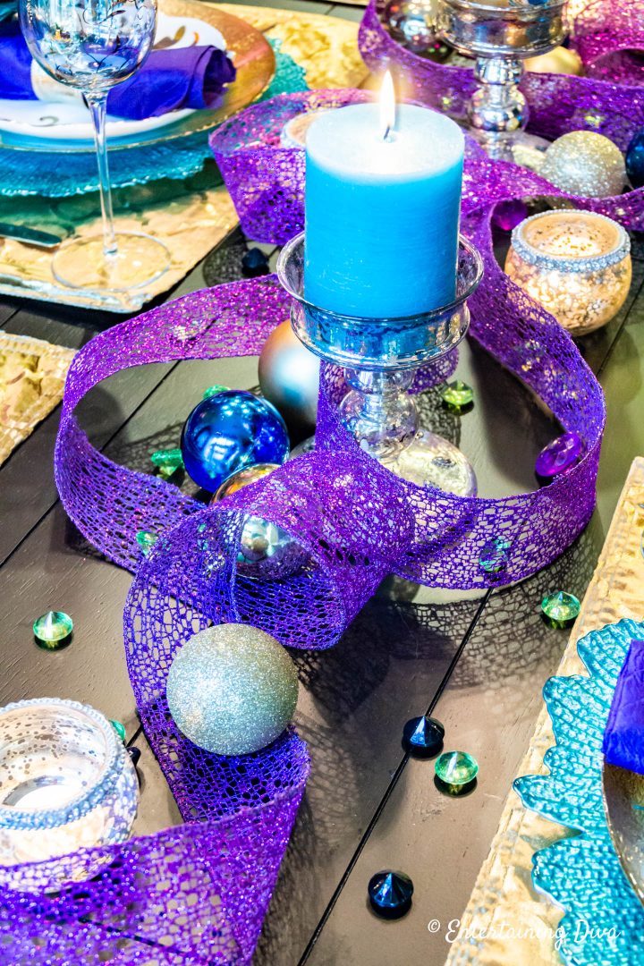 Teal candle with purple wired ribbon and gold Christmas ornaments in a peacock-inspired tablescape centerpiece