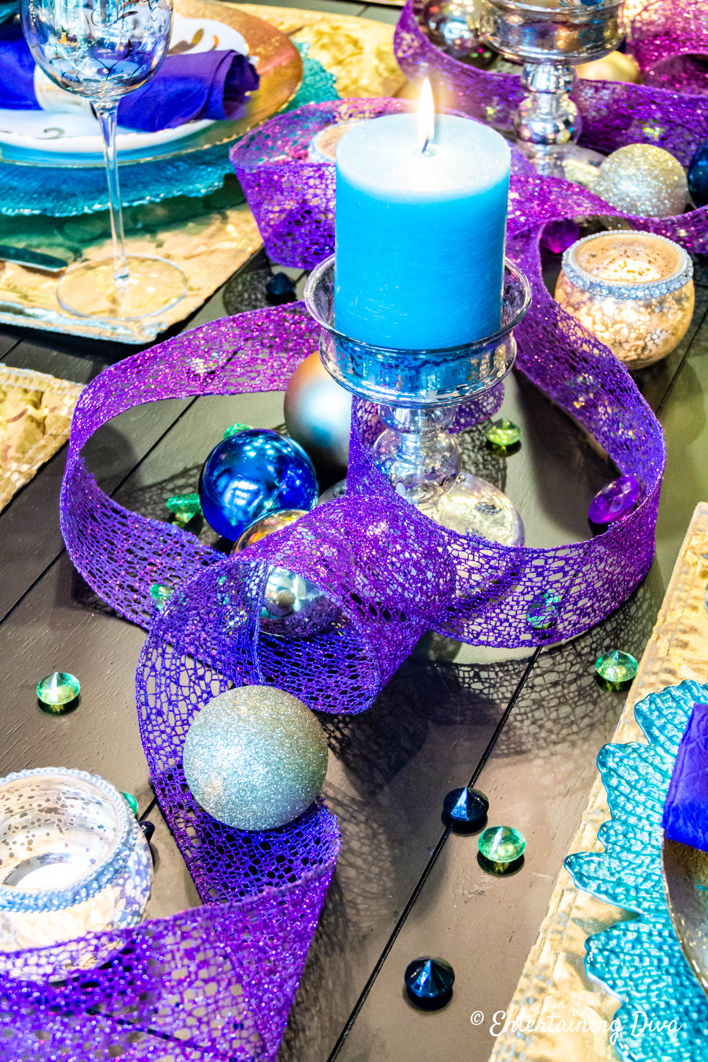 Teal candle with purple wired ribbon and gold Christmas ornaments in a peacock-inspired tablescape centerpiece