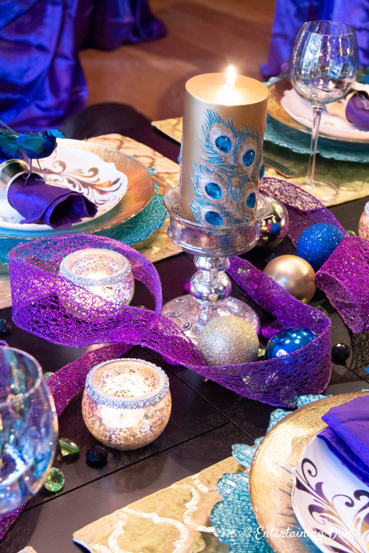 Gold and teal peacock pillar candle with purple wired ribbon as a Mardi Gras centerpiece