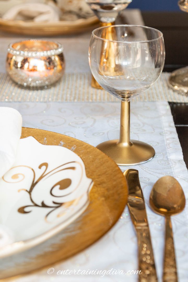gold dipped wine glass on a table with a gold charger, white and gold plates and gold cutlery