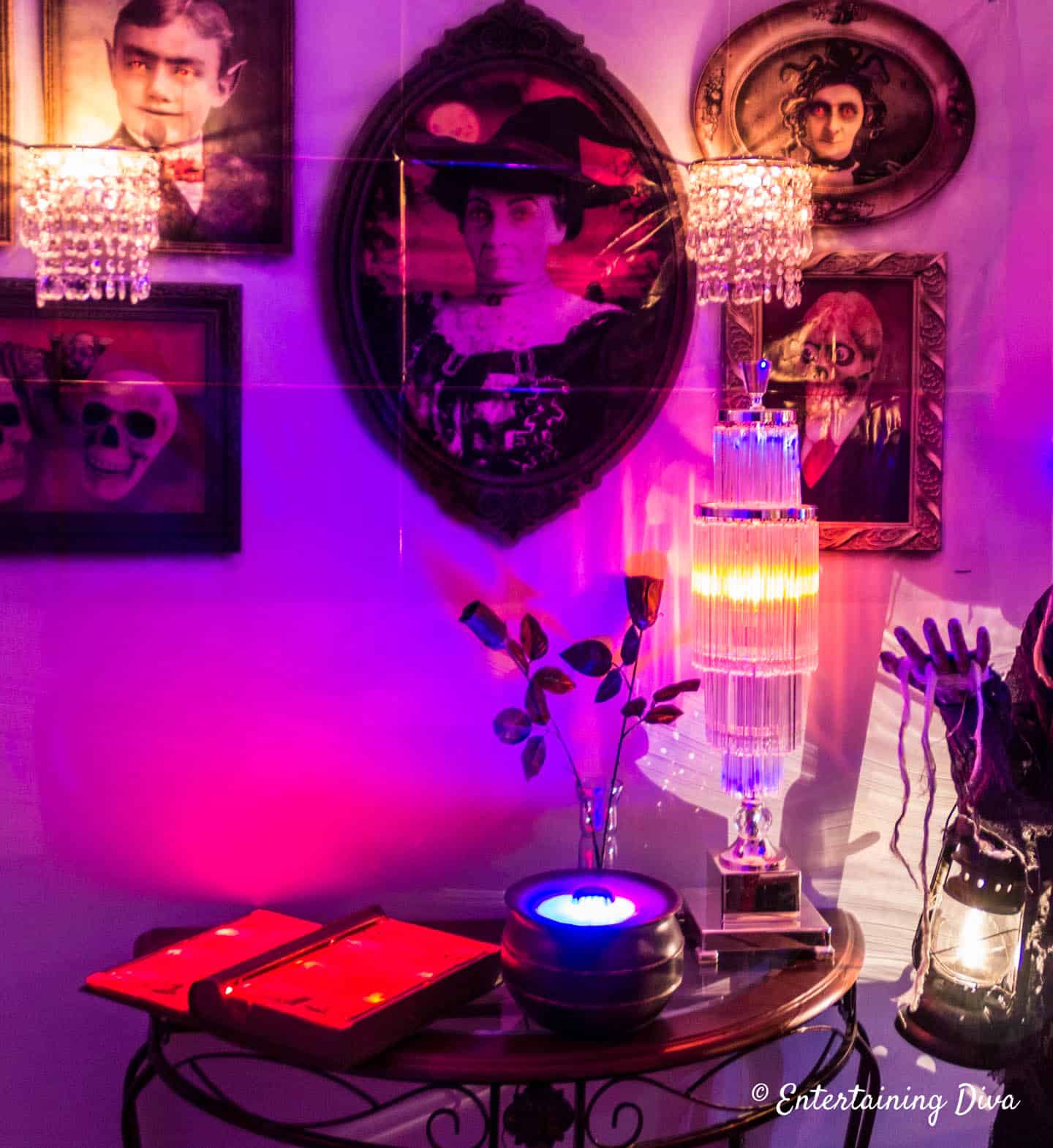Lighted Halloween props (spell book and misting witch cauldron) on a table below some haunted pictures