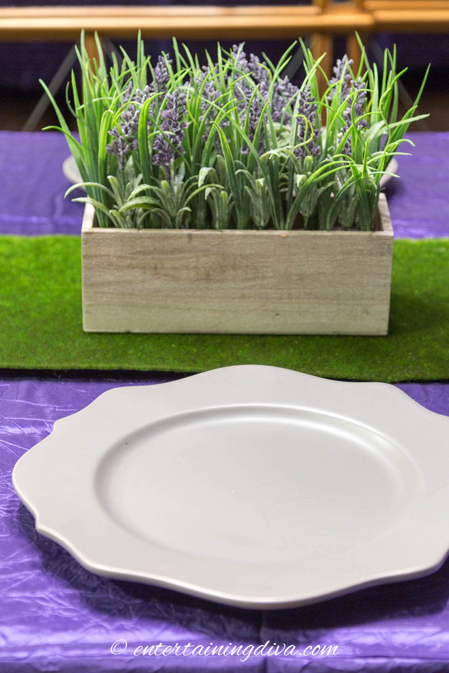 A gray charger on a purple tablecloth in front of a green and purple centerpiece