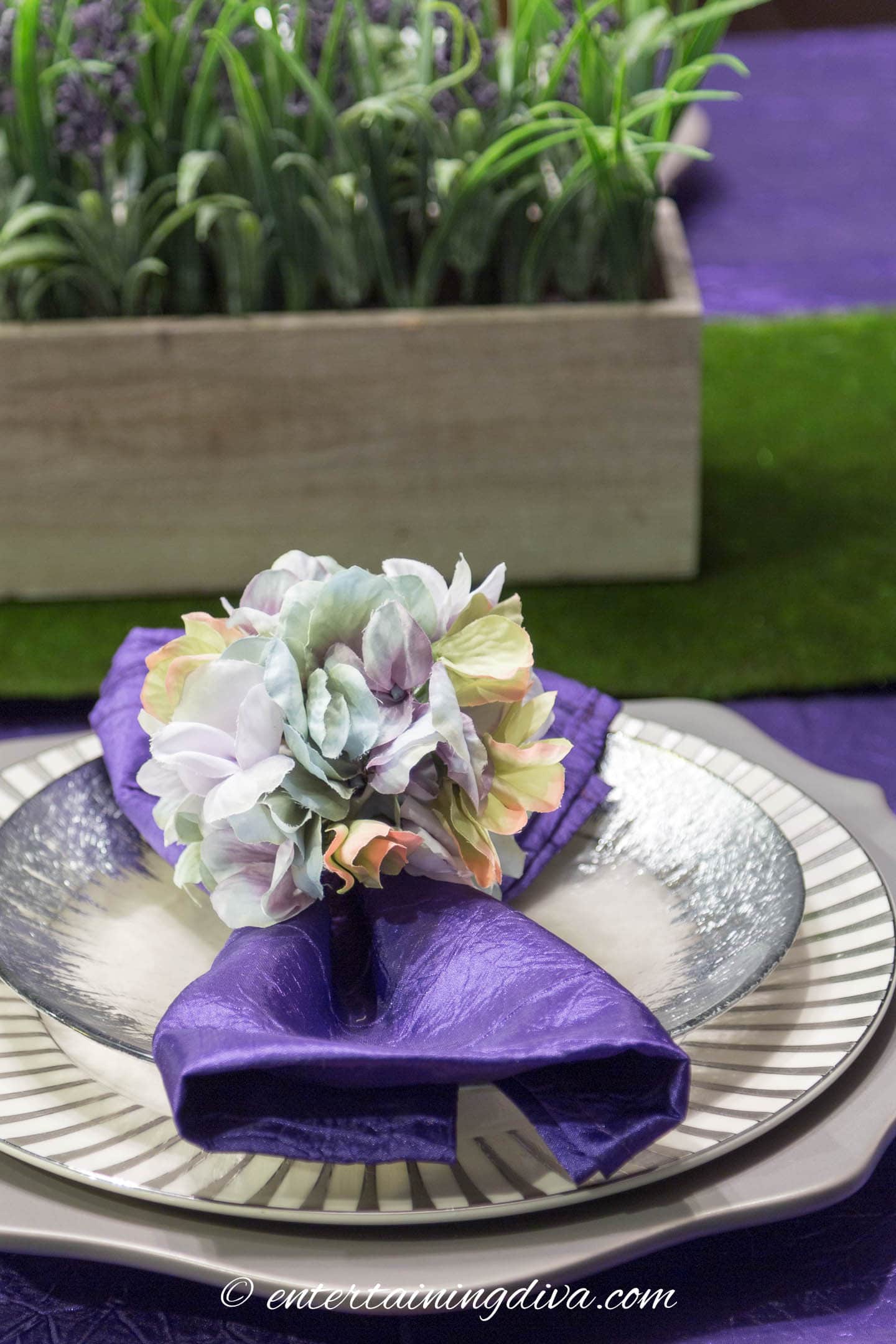Close up of a floral napkin ring holding a purple napkin on a silver and white place setting