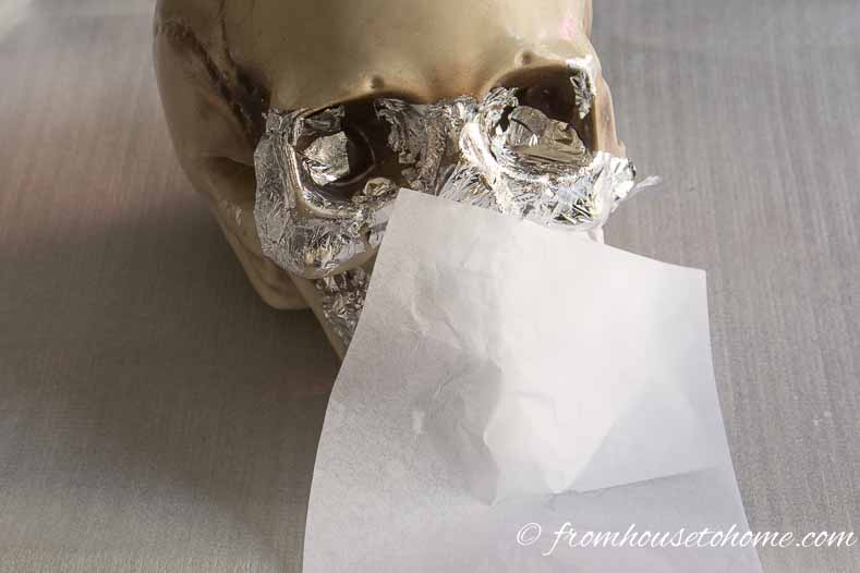 Plastic skull half covered with silver leaf and a piece of tissue paper