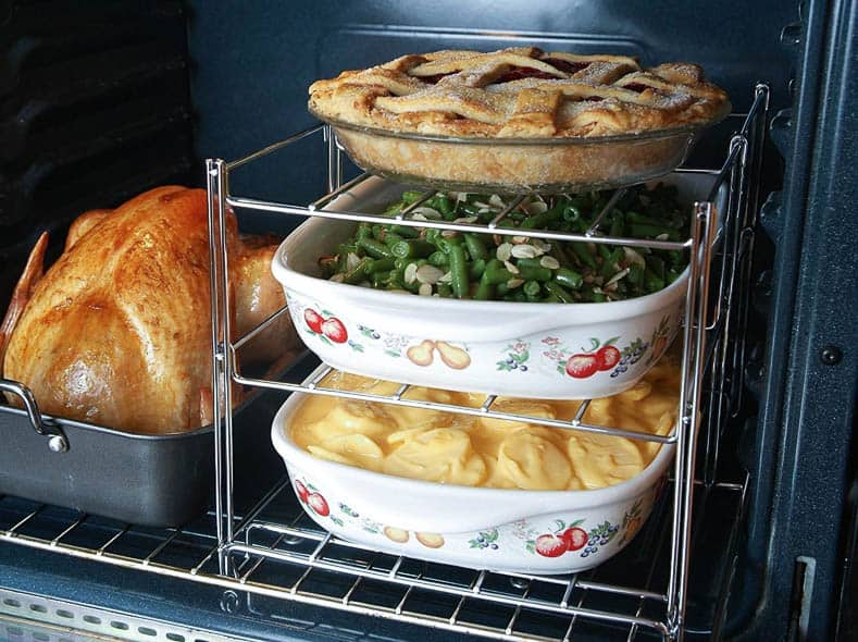 Tiered oven rack with a pie, green pies and scalloped potatoes beside a pan with a turkey