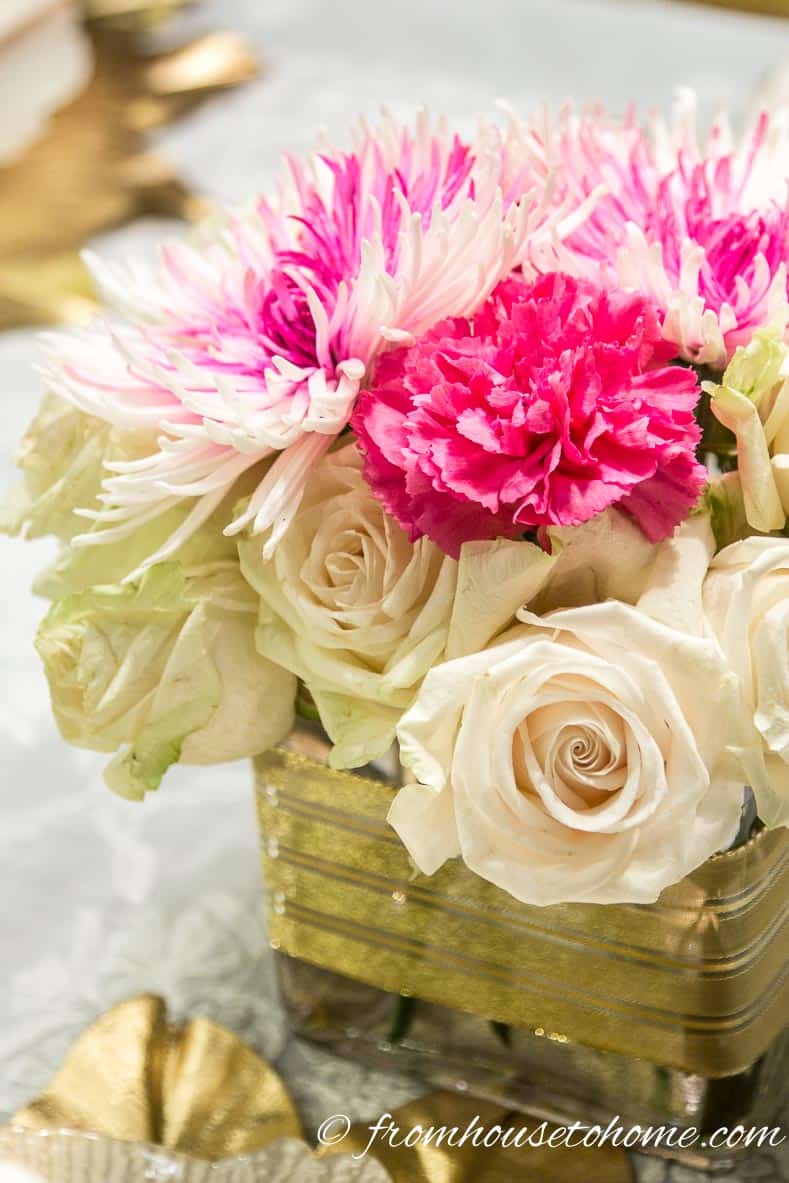 White and pink flowers in a square vase wrapped in gold ribbon