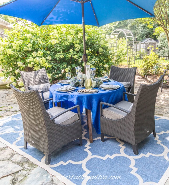 An outdoor table setting with a blue umbrella that matches the tablecloth and area rug