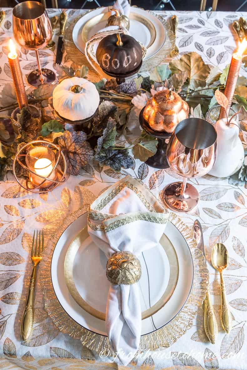 Gold and copper fall table setting with white and black mini pumpkins in the centerpiece