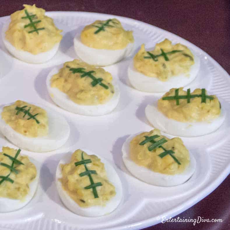 Devilled eggs that look like footballs with green onion laces on an egg plate