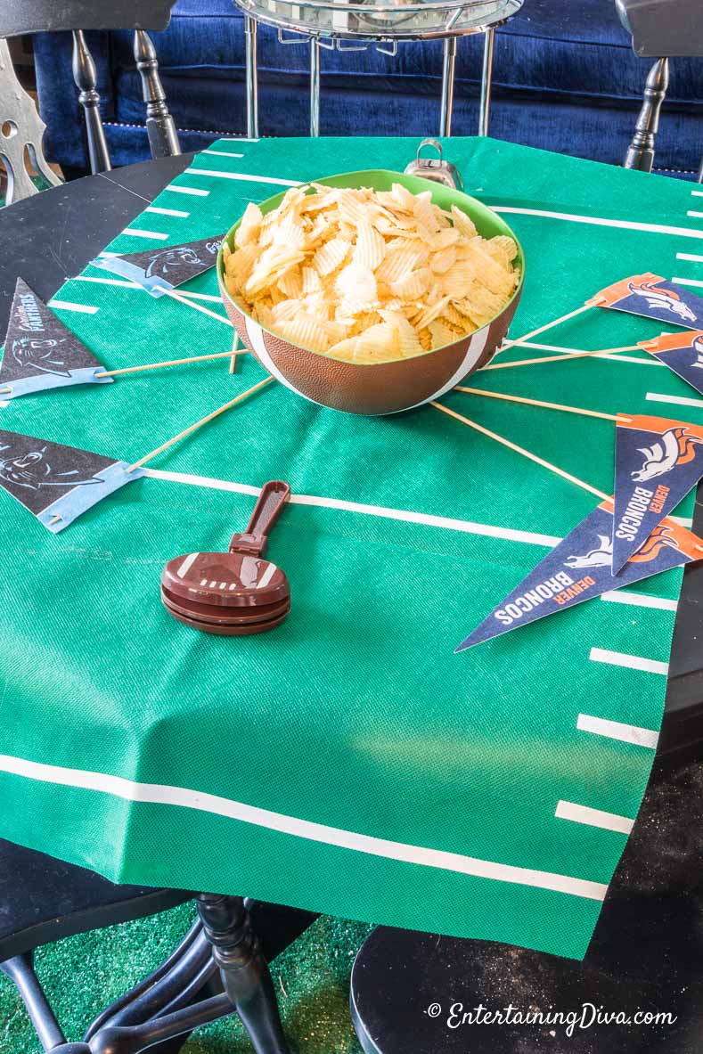 Football-shaped bowl with chips, a football noise maker, and football team flags on a table with a Football field table runner