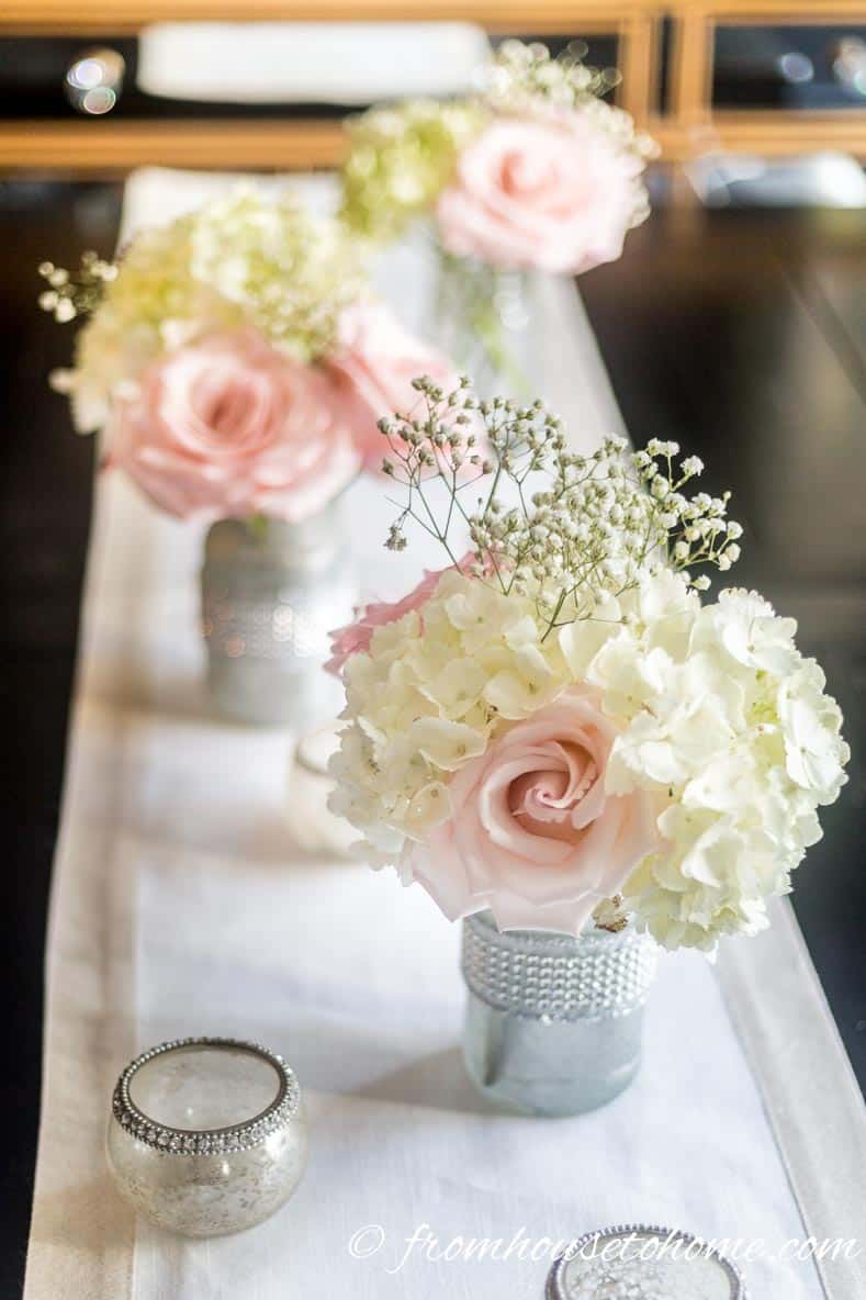 Elegant pink floral centerpiece made from silver-painted mason jars holding white hydrangeas, pink roses and white baby's breath