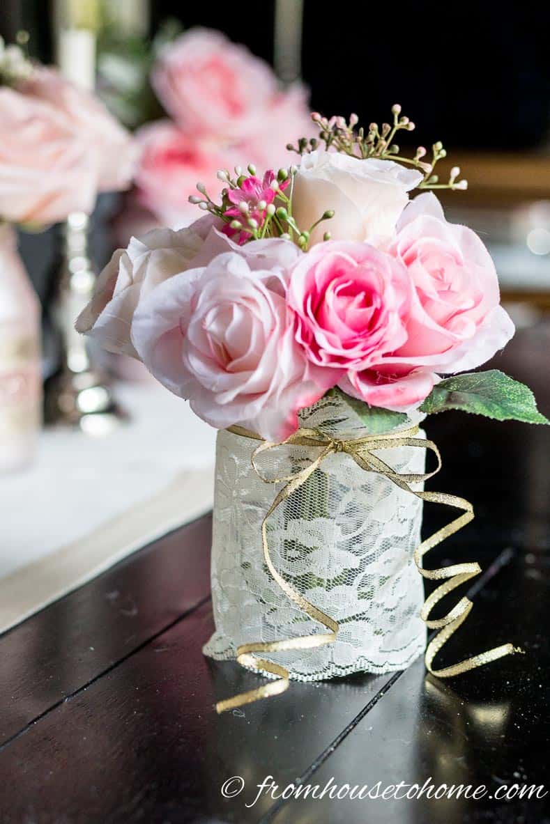 DIY pink flower centerpiece made with a mason jar wrapped in white lace and a gold ribbon