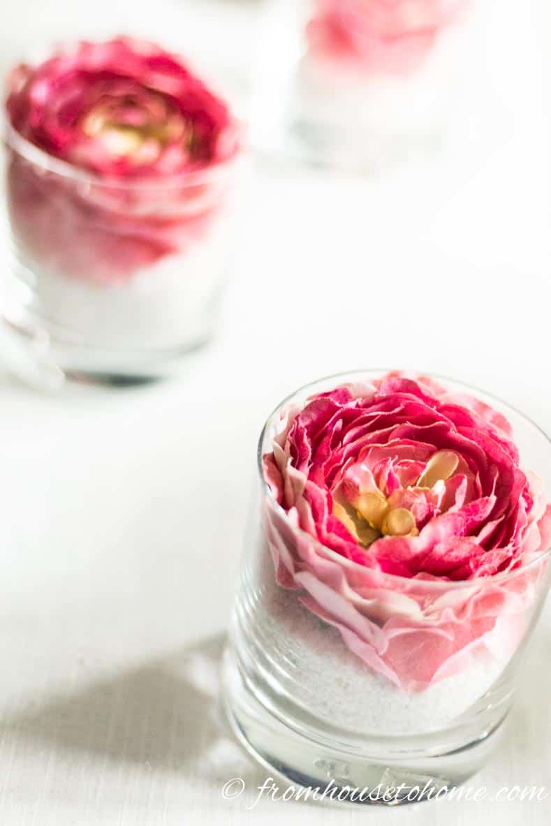 A simple but elegant DIY pink flower centerpiece made with pink floral napkin rings in a glass with white sand