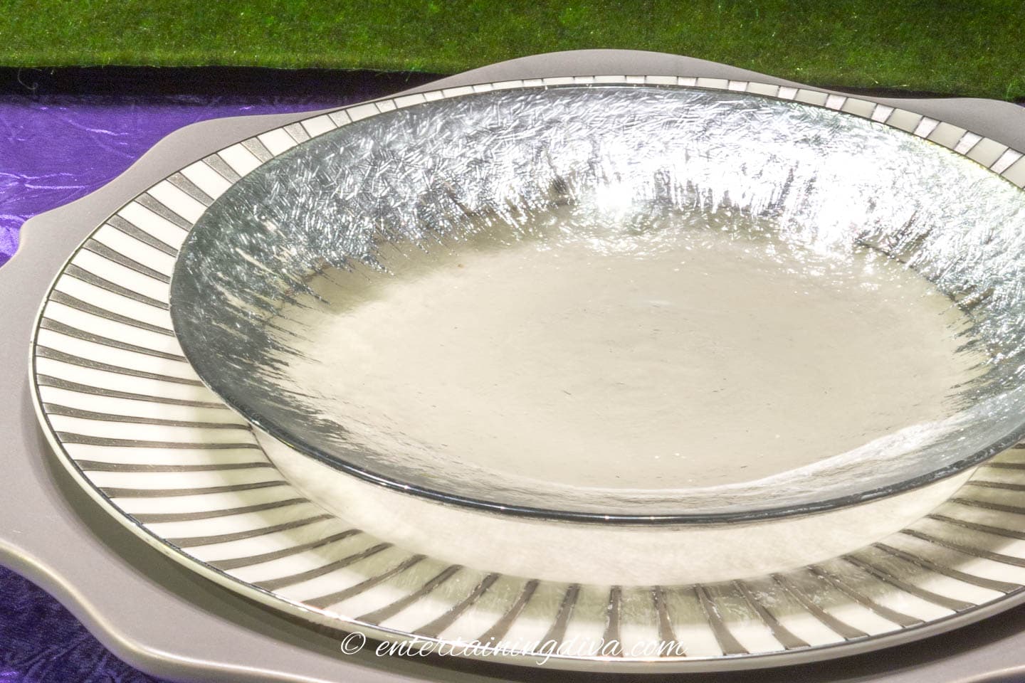 Silver-edged glass appetizer plate on top of a white and silver dinner plate on a gray charger