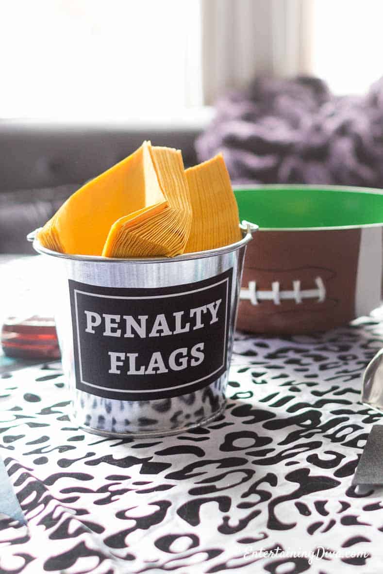 football party decor made with yellow napkins in a galvanized pail with a label that says penalty flags