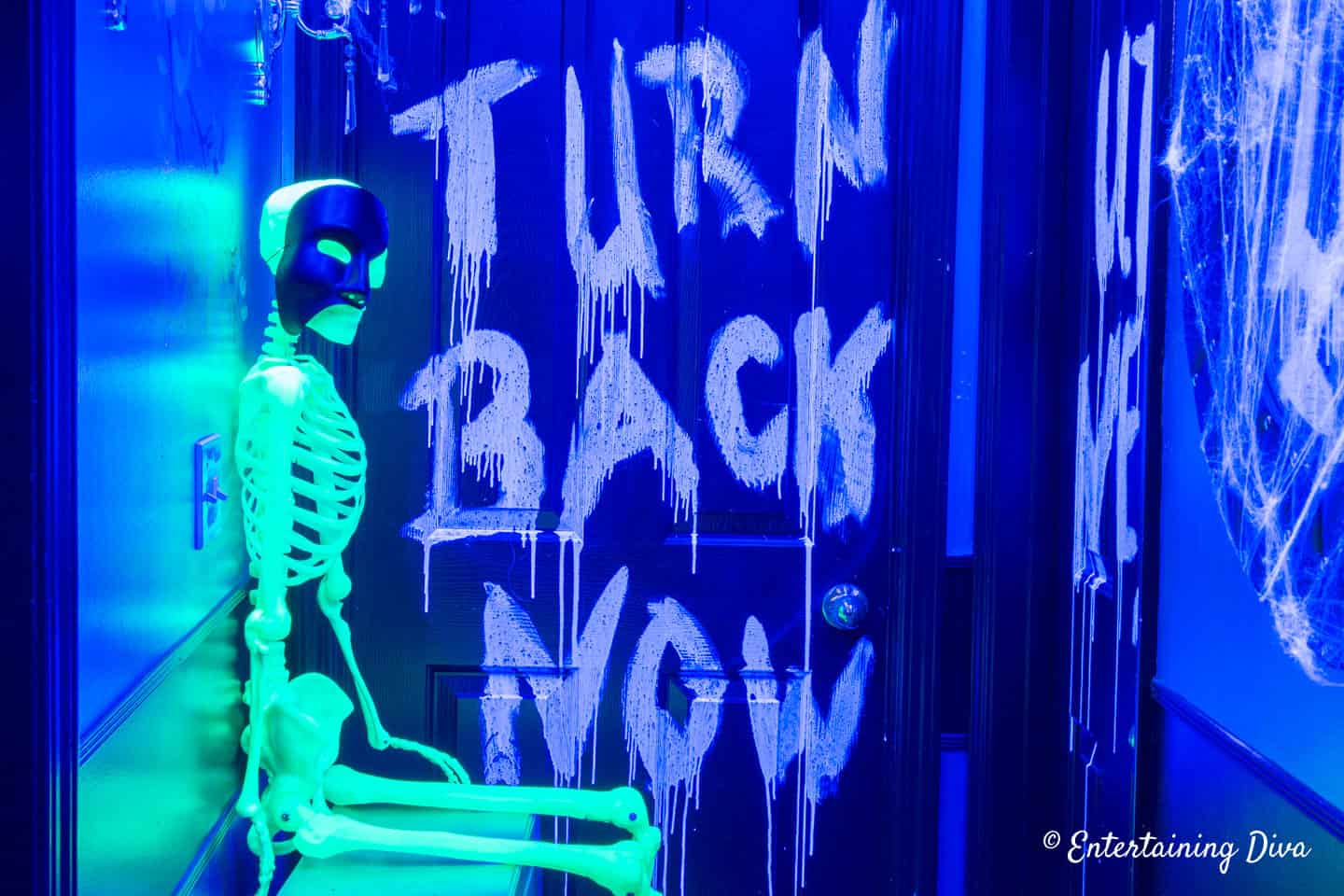 Turn Back Now sign on a door and a glow in the dark skeleton lit by black light