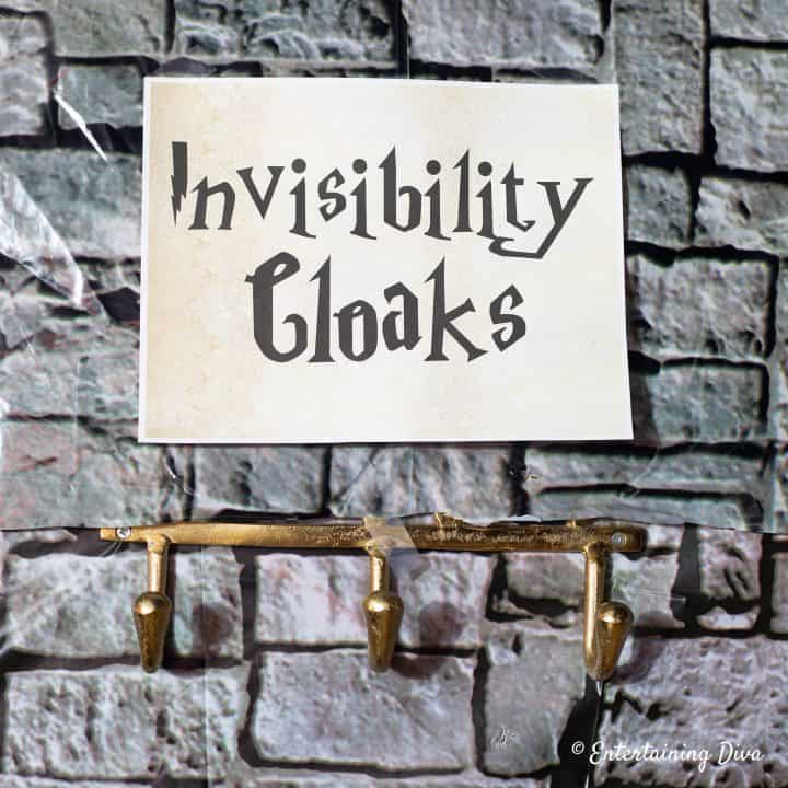 Invisibility cloaks printable sign hung on a wall covered with a stone scene setter for a Harry Potter party