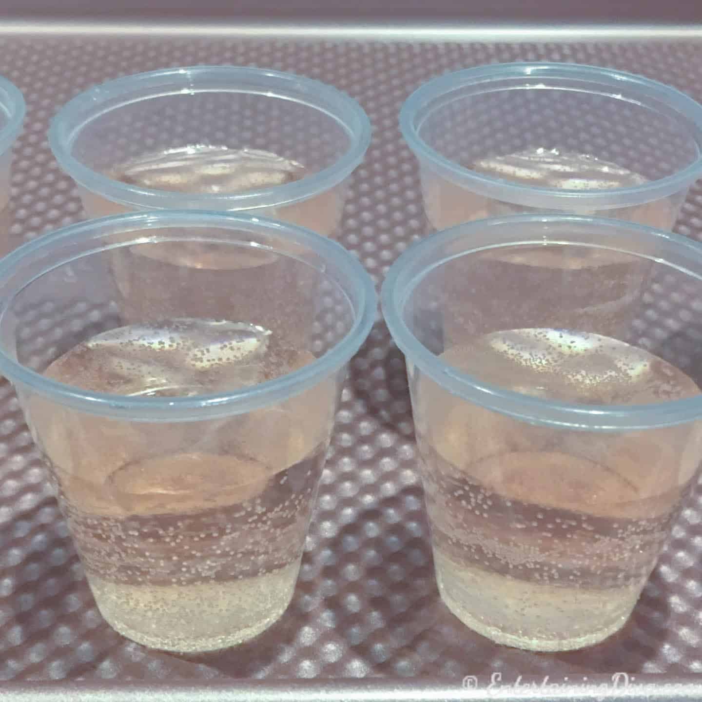 Pink champagne jelly shots in shot cups on a cookie sheet