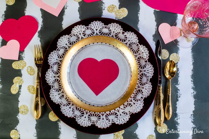 Valentine day table setting with white paper doily on a red charger plate and gold cutlery